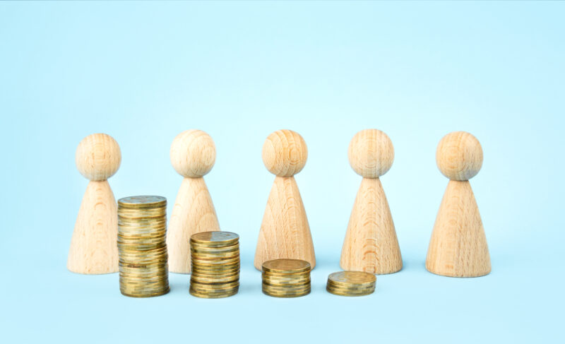 Wooden figures of people representing the process of raising money to buy a business with four coin piles growing from one side to the other. 