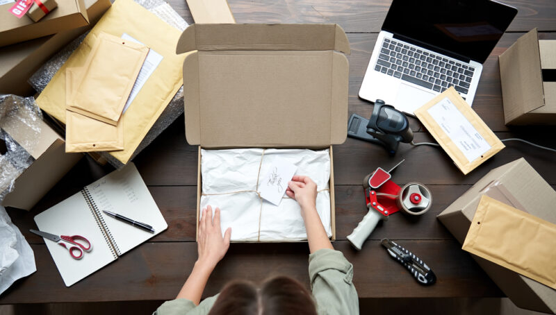Woman in eCommerce packing a package, representing the potential of online businesses as alternative investments